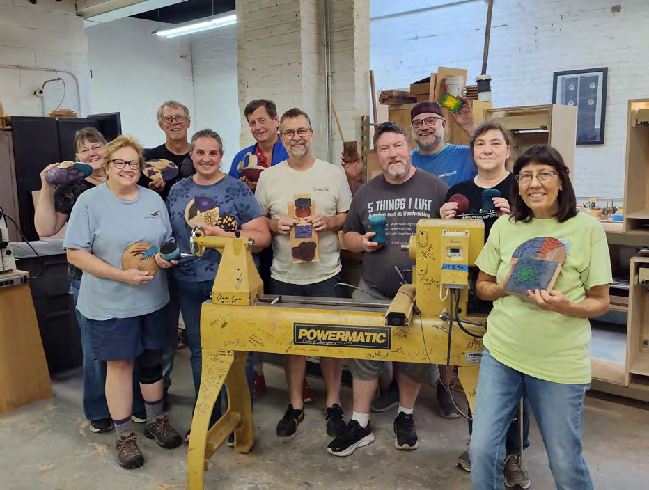 Chicago Woodturners members gathered around a lathe holding recent work